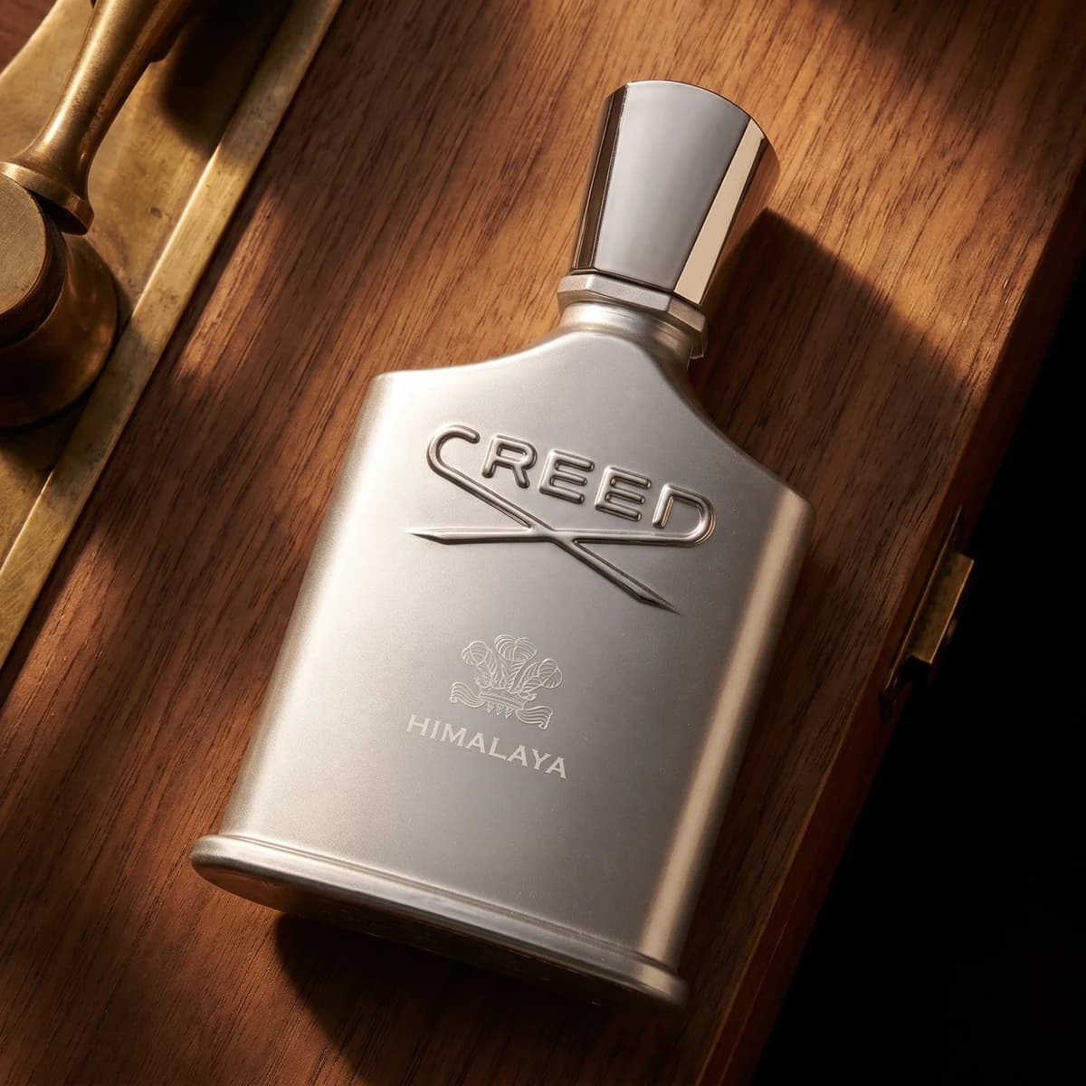 A silver bottle of Creed Himalaya lying on a polished wooden box