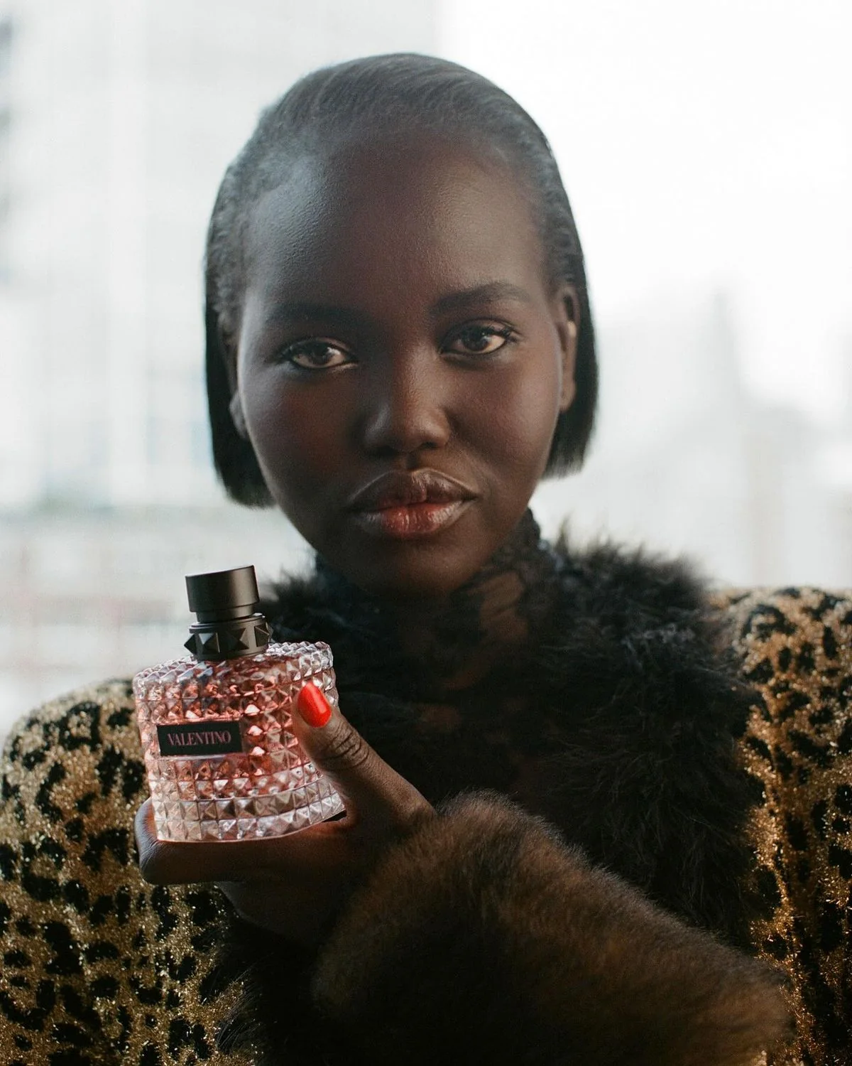 A woman in a leopard-print coat holding a pink bottle of Valentino Donna Born in Roma Coral Fantasy